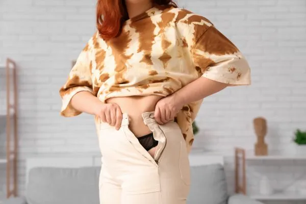 Image of woman trying to do her trousers up after pregnancy weight gain Welwyn Garden City